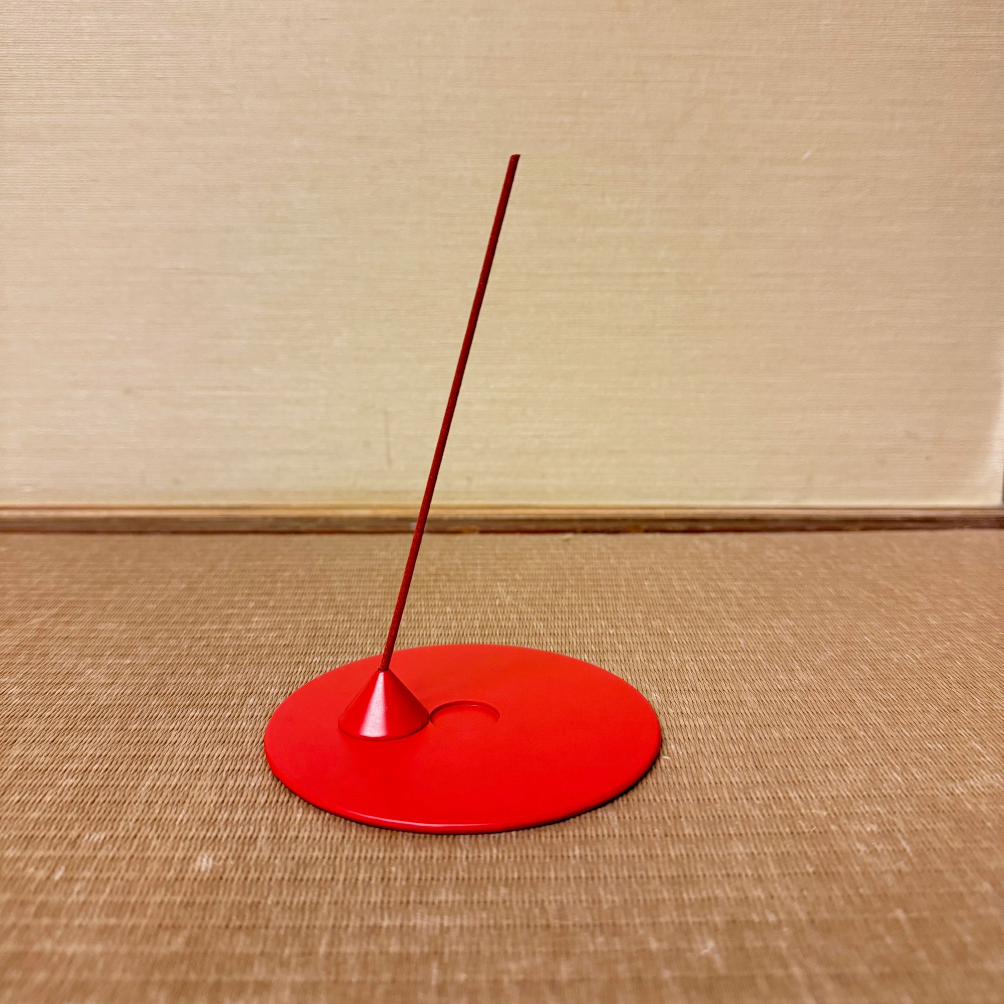 Red incense holder with a single incense stick on a wooden floor.