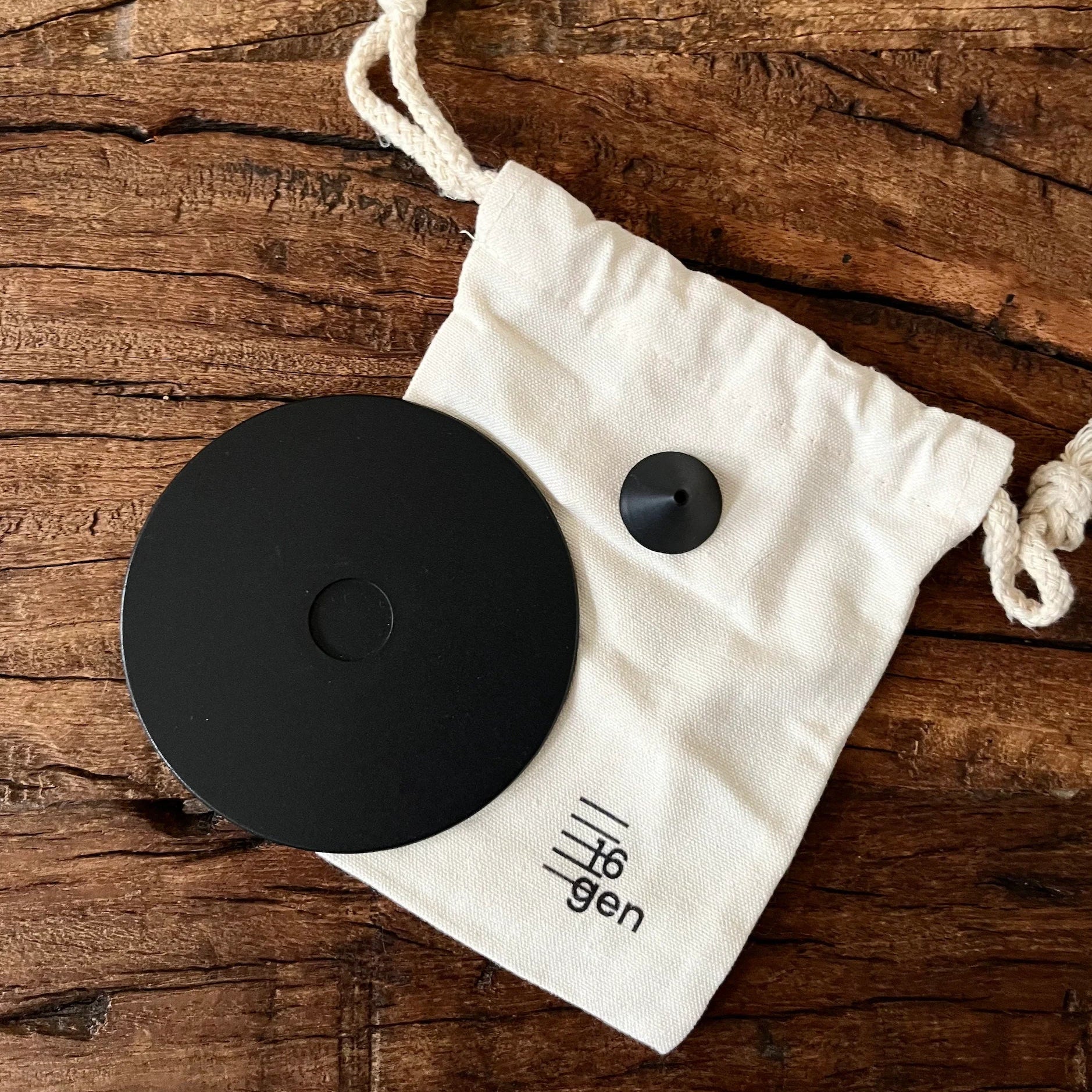 Black circular object with a smaller black object on a white drawstring bag on a wooden surface.